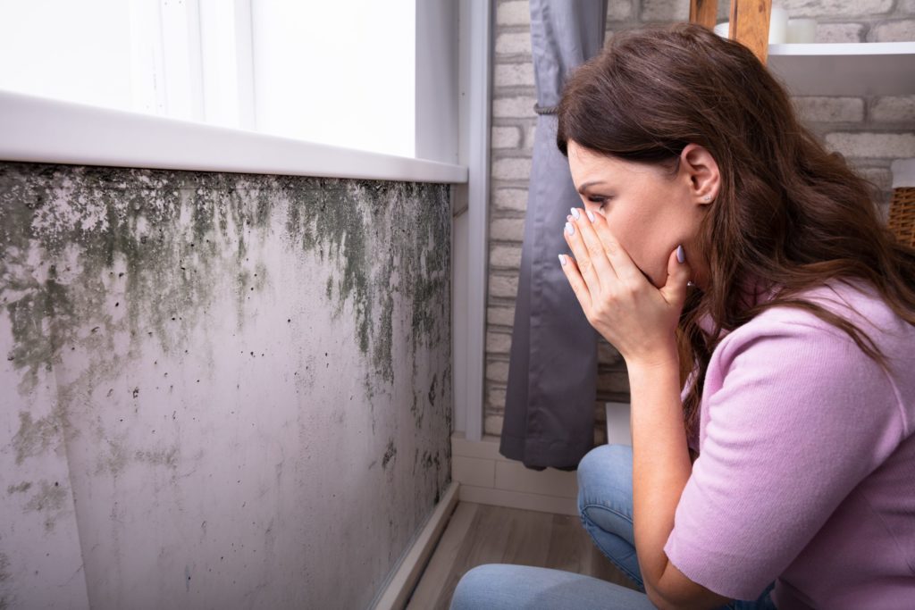 woman covering her face worried looking at a wall with mold
